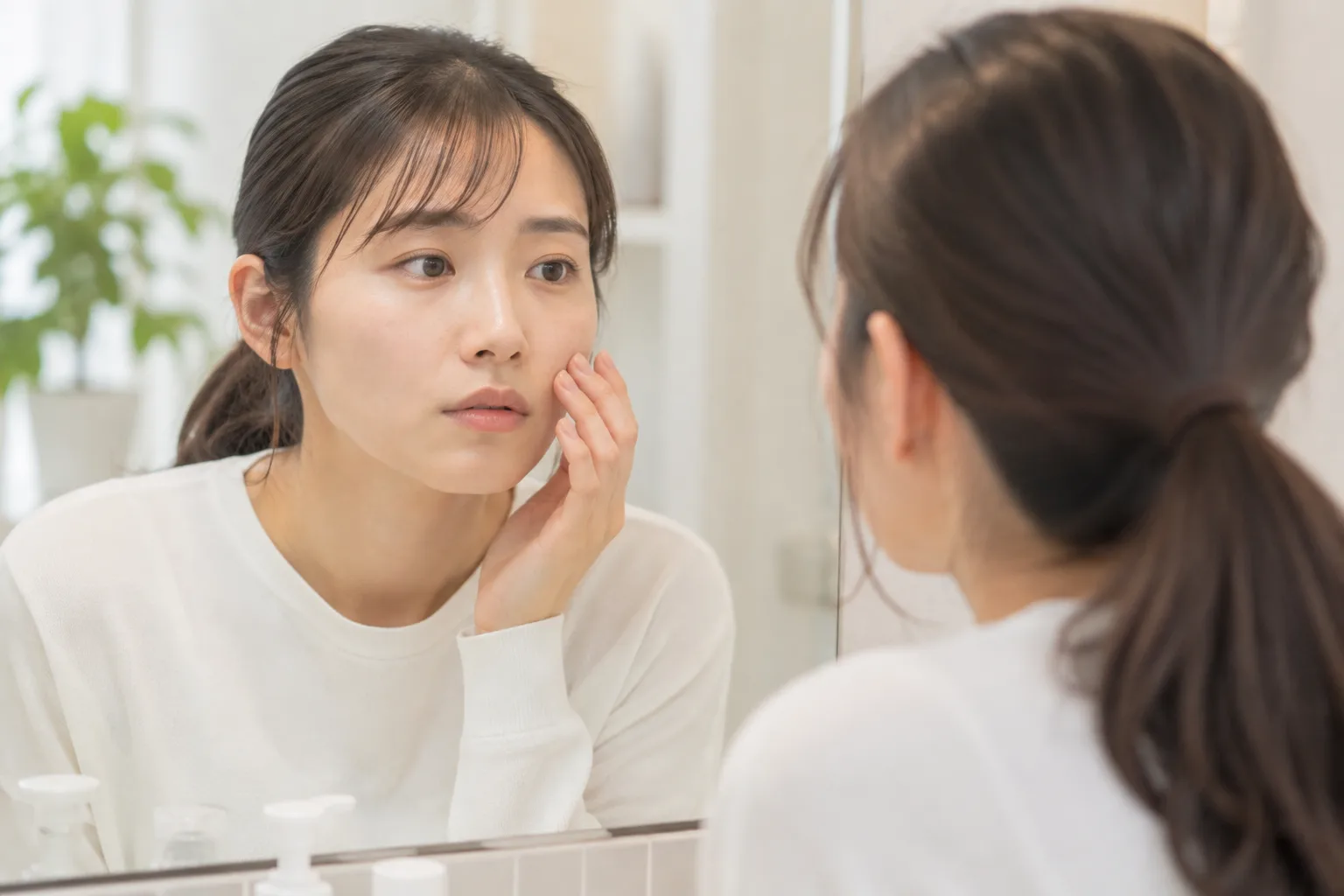 鏡越しに頬の肌の質感を指先で確認する女性