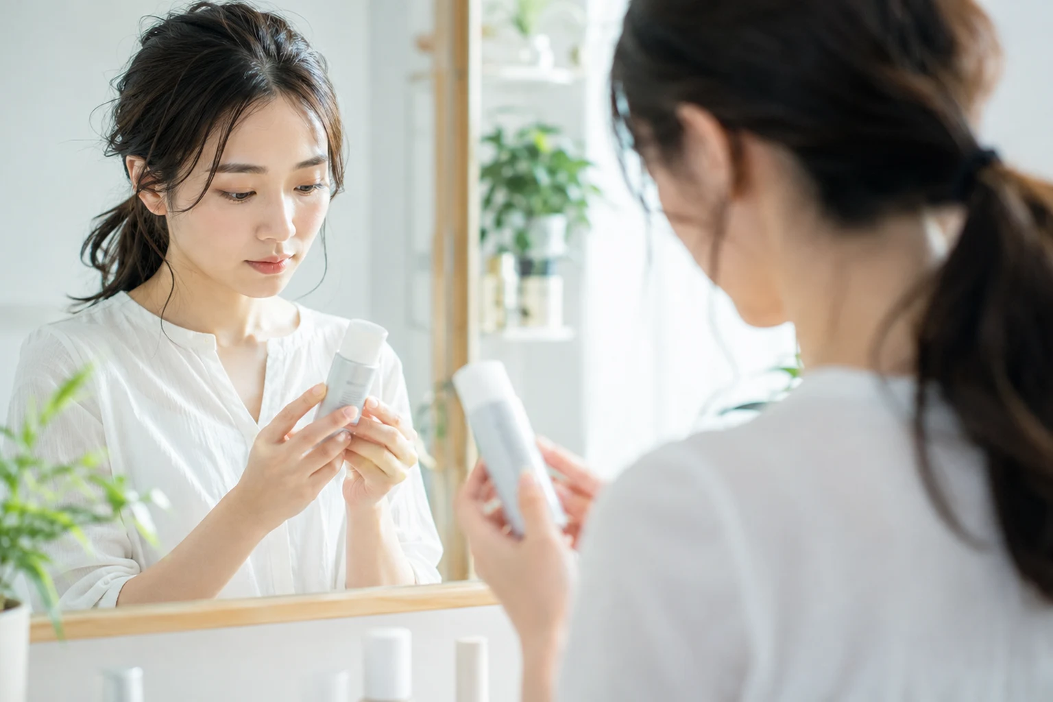 洗面所で日焼け止めのパッケージ裏面表示を鏡越しに確認する女性